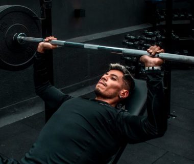 Man performing bench press with heavy barbell in a gym setting, focusing on strength training.